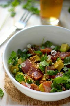 a white bowl filled with lots of food next to a fork and glass on top of a table