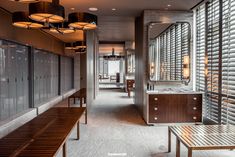 an empty bathroom with wooden benches and large mirrors on the wall, along with windows covered in blinds