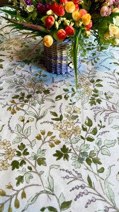 a basket filled with lots of colorful flowers on top of a white table covered in green leaves