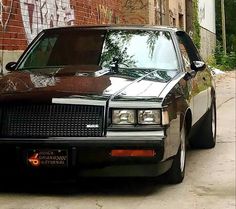 a black car parked on the side of a road next to a brick wall with graffiti