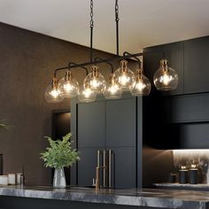 a kitchen island with lights hanging from it's ceiling and a potted plant on the counter