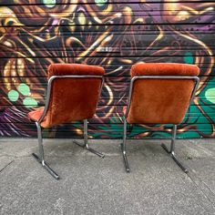 two chairs sitting next to each other in front of a wall with graffiti on it