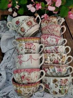 a pile of cups and saucers sitting on top of a lace covered table cloth