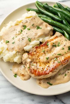 chicken with gravy, mashed potatoes and green beans on a white plate