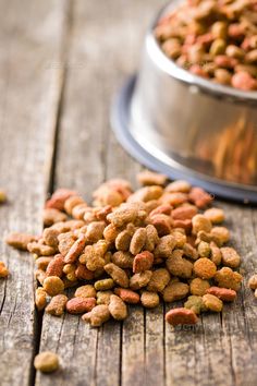 a pile of cat food sitting on top of a wooden table next to a metal bowl