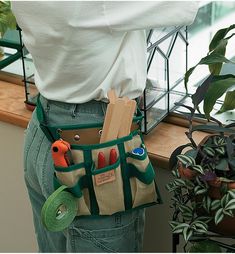 a person is holding a tool belt with tools in it and some plants behind them