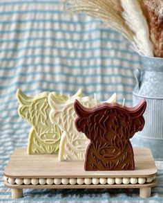 three cookies shaped like animals on a wooden tray next to a vase with dried grass in it