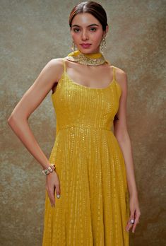 Shine effortlessly with this stunning Yellow and Gold Sequin Embroidered Anarkali Gown, crafted from a luxurious viscose georgette. The vibrant yellow anarkali features a chic strappy round neckline, exuding elegance with intricate sequin and threadwork embroidery that catches the light beautifully with every movement. A sophisticated back cutout at the waist adds a modern twist, perfectly balancing tradition with contemporary flair. The look is completed with a matching net dupatta adorned with delicate embroidered scallop lace, ensuring a flawless look. Ideal for Haldi, Mehndi, Sangeet events, or as an eye-catching wedding guest attire, this gown is designed to make you stand out effortlessly. Composition : Anarkali - Viscose Georgette and Dupatta - Soft net Care: Dry Clean Only and Vacu Traditional Yellow Maxi Dress For Festive Occasions, Designer Yellow Georgette Gown, Yellow Georgette Dress With Mirror Work, Yellow Georgette Gown For Diwali, Yellow Anarkali Set With Cutdana For Party, Yellow Anarkali Set With Chikankari Embroidery For Reception, Yellow Georgette Gown For Festive Occasions, Elegant Yellow Georgette Anarkali Set, Yellow Georgette Gown For Eid