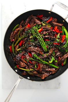 beef and broccoli stir fry in a wok with sesame seeds on the side