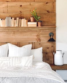 there is a bed with white pillows and books on the headboard, next to a wooden shelf