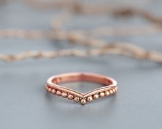 a rose gold ring with beaded edges on a gray surface, resting on a string