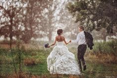 a bride and groom walking in the rain holding hands with each other on their wedding day