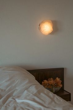 a light that is on the side of a wall above a bed with white sheets