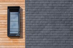 a black window on the side of a wooden building next to a gray brick wall