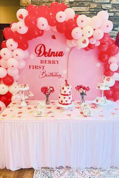 a table topped with lots of red and white balloons next to a pink backdrop that says denna berry first birthday