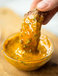 a person dipping something into a small bowl filled with mustard and green stuff in it