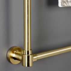 a close up view of the handles on a bathroom towel rack in gold metal with a marble tile wall behind it