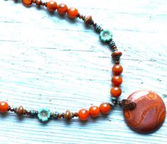 18"   Agate necklace made w/rustic red orange Jasper gemstone pendant,  8 mm Carnelian colored Agate beads, 4 mm Carnelian colored agate beads, 12 mm aqua & rustic red Lampwork accent beads, 8 mm accent Picasso glass beads, patina turquoise Bali style accent beads, 10 mm green Picasso flower glass accent beads, 6 mm caramel Picasso beads w/aqua finish, 3 mm patina turquoise disc spacers, 3 mm Picasso glass beads, antique brass bead caps, brass spacer beads and brass lobster claw clasp. Handmade Earthy Turquoise Necklace For Gift, Rustic Turquoise Necklace With Natural Stones For Gift, Orange Bohemian Jewelry With Round Pendant, Orange Bohemian Round Pendant Jewelry, Bohemian Orange Round Pendant Jewelry, Turquoise Agate Necklace With Round Beads As Gift, Bohemian Rust Necklace With Natural Stones, Artisan Rust-colored Necklace For Gifts, Bohemian Rust Necklaces For Gift