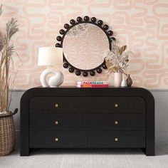 a dresser with a mirror, vases and plants on it in front of a wallpapered background