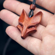 a hand holding a wooden pendant with a fox head on it's side and a black cord