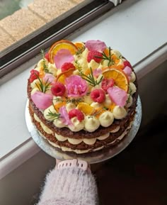 a cake with fresh fruit and flowers on top is being held by someone's hand