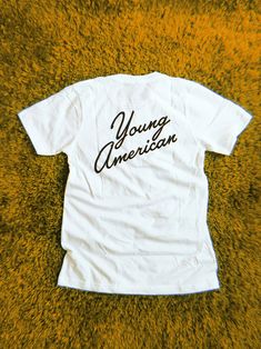 young american tee Black Cotton T-shirt With Letter Print, Cotton T-shirt With Black Letter Print, Black Print Crew Neck T-shirt For Streetwear, Cotton Graphic Design Tops For Fan Merchandise, White Graphic Print Top For Fan Merchandise, Unisex Graphic Print Tops For Fan Merchandise, Cotton Graphic Tee With Letter Print, Pre-shrunk White Print Graphic Tee, Relaxed Fit Graphic Design Top For Fan Merchandise