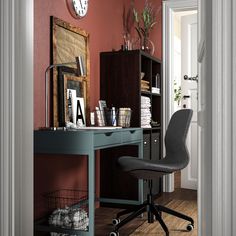 a desk with a chair and a clock on the wall in a room that has red walls