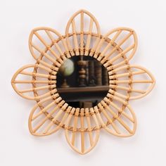 a round mirror with wooden handles and an intricate design on the front, against a white wall