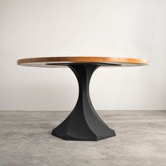 a round wooden table sitting on top of a cement floor next to a white wall