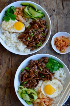 two bowls filled with rice, meat and veggies on top of a wooden table