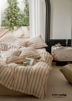 an unmade bed with striped sheets and pillows on the floor next to a mirror