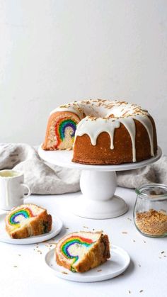 a bundt cake with white icing and rainbow designs on it, next to two slices