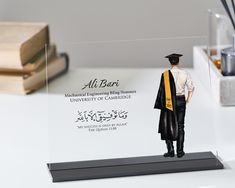 a figurine of a man wearing a graduation cap and gown standing on a desk