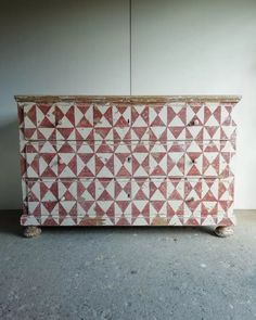 a red and white chest with triangles painted on the front, sitting in a room