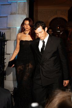 a man in a suit and woman in a black dress walking down the red carpet