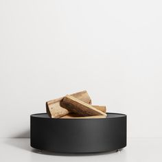 a black bowl with some pieces of wood in it on top of a white table