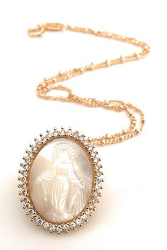 "Virgen la Milagrosa Necklace This eye-catching 1mm 18k gold plated Saturn chain hangs a gorgeous mother of pearl carved oval shape Miraculous Virgin Mary image with luminous clear cubic zirconia stones around it. This necklace is designed to be worn all day. Would be a perfect bride accessory, a gift for your wife, mother, sister, grandmother or as a gift for yourself. DETAILS: Necklace length: 17.5\" inches / 45 cm Pendant diameter: 0.9\"x \"1 inches / 2 x 2.5 cm Other Miraculous Medals are av Miraculous Medal Necklace For Mother's Day Gift, Miraculous Medal Jewelry Gift For Mother's Day, Mother's Day Gift Jewelry With Miraculous Medal, Elegant Miraculous Medal Necklace, Gold Cameo Round Pendant Jewelry, Elegant Miraculous Medal Jewelry For Gift, Elegant Oval Miraculous Medal Jewelry, Elegant Miraculous Medal Jewelry, Elegant Miraculous Medal Jewelry Gift