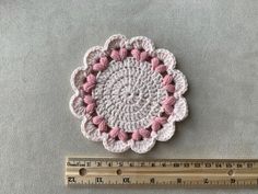 a crocheted doily sits next to a ruler on a gray surface,