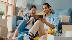 a man and woman sitting on the floor looking at an electronic device together in their living room