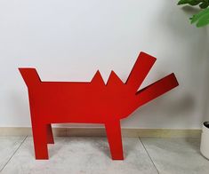 a red sculpture is sitting on the floor next to a potted plant and a white wall