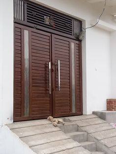 two brown wooden doors sitting on the side of a white building next to steps and stairs