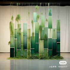 an art installation made out of green glass blocks and plants hanging from the ceiling in front of a white curtain