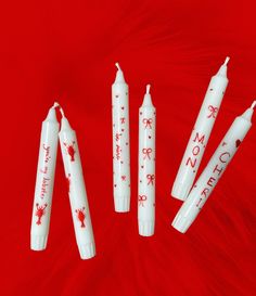 four white candles with red writing on them sitting next to each other in front of a red background