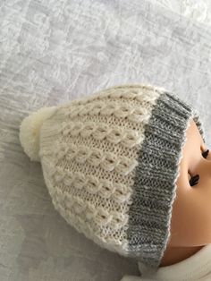 a doll wearing a knitted hat on top of a white bed sheet and pillow