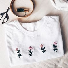 a white t - shirt with pink flowers on it next to some scissors and thread