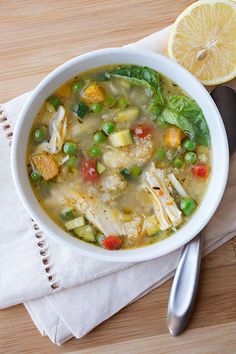 a white bowl filled with chicken and vegetable soup next to a slice of lemon wedge