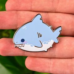 a hand holding a blue and white pin with a shark on it's back