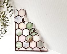 a piece of stained glass hanging from the side of a white wall next to a potted plant