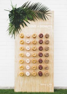 a wooden board with doughnuts on it next to a palm tree and white brick wall