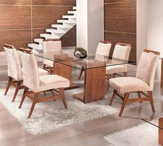 a glass dining table surrounded by beige chairs and white rugs with stairs in the background